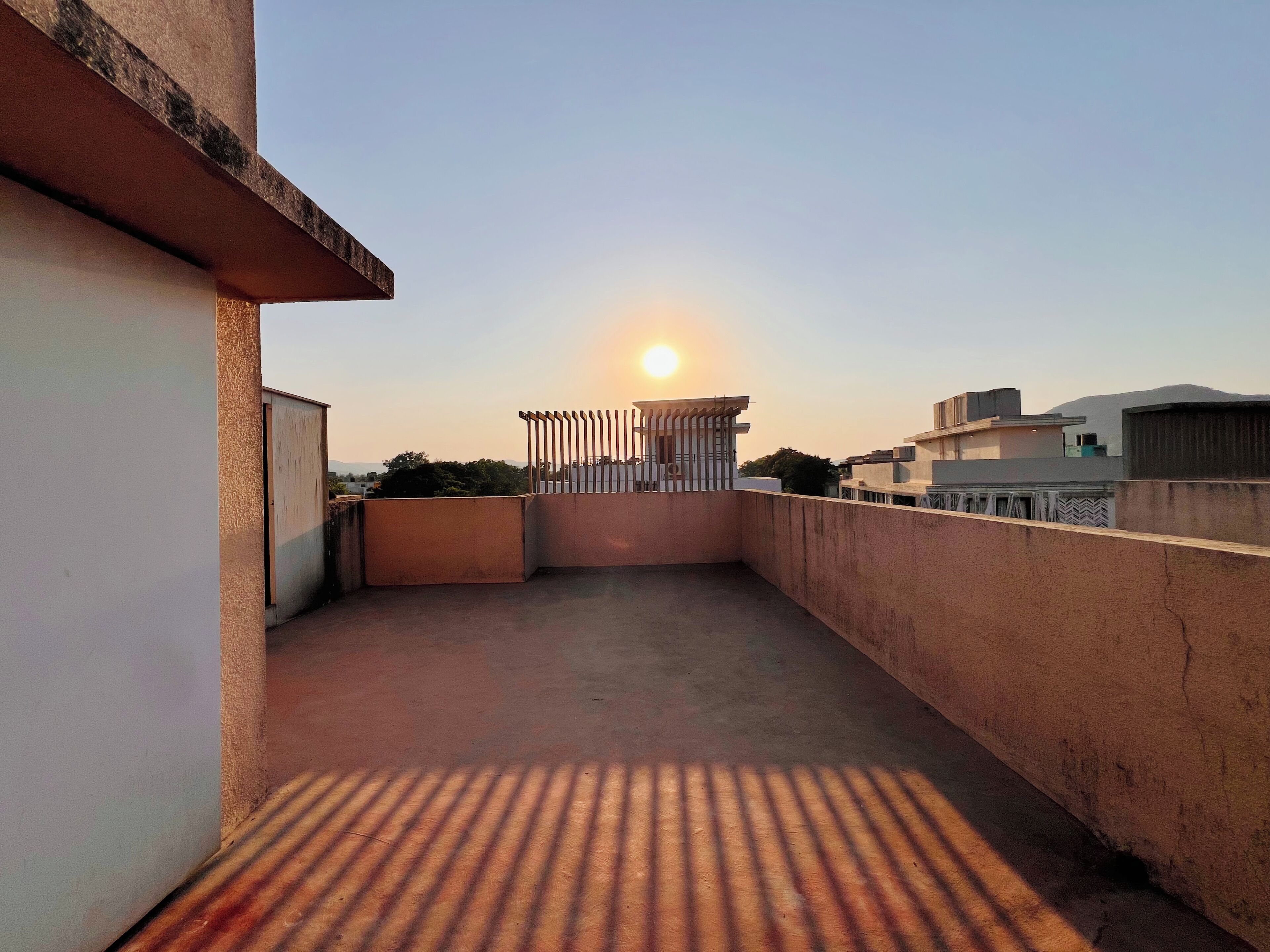 A rooftop terrace with a view of the sunset, a metal gate, and a concrete floor.