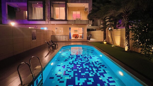 A modern two-story house with a swimming pool, outdoor seating, and a well-lit entrance.