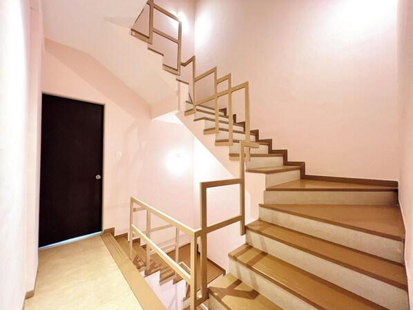 A staircase with a geometric railing design, a dark door, and a light-colored floor.