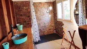 Une pièce avec un mur en briques, un plancher en bois, une fenêtre avec des rideaux, un luminaire suspendu et une petite table sur laquelle se trouve un récipient bleu.