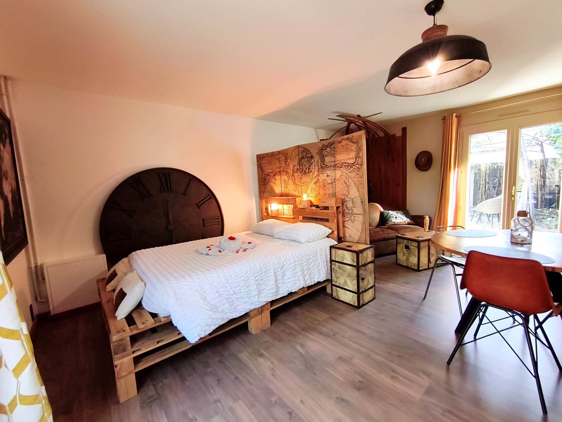 A room with a bed, a wooden headboard, a map wall, a table with chairs, and a window.
