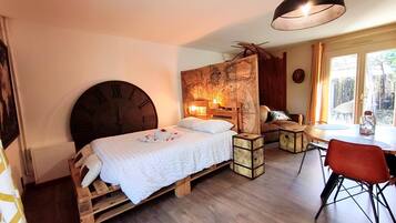 A room with a bed, a wooden headboard, a map wall, a table with chairs, and a window.