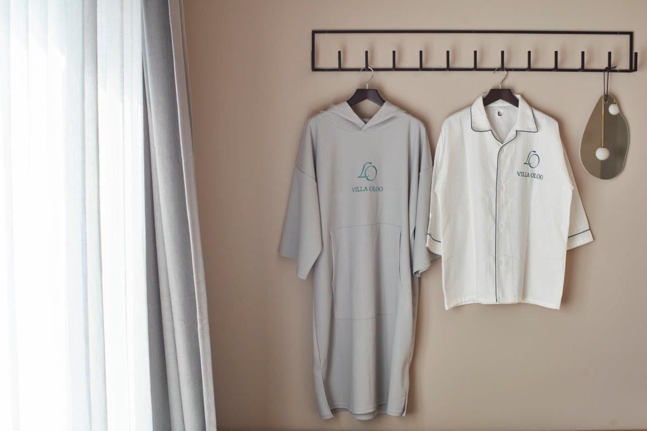 Two white shirts with 'Villa Olcoo' logo on a wall-mounted rack.
