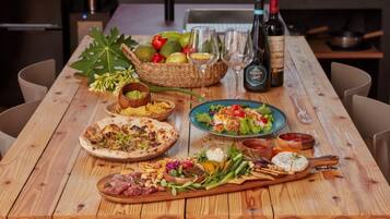 A wooden table with various food items, including pizza, salad, and charcuterie, along with wine bottles and glasses.