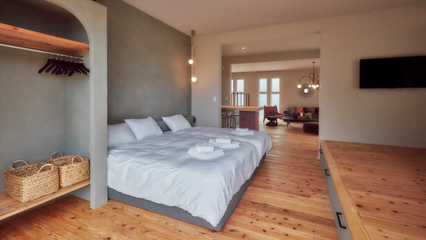A modern bedroom with a large bed, wooden flooring, a built-in bench, and a flat-screen TV mounted on the wall.