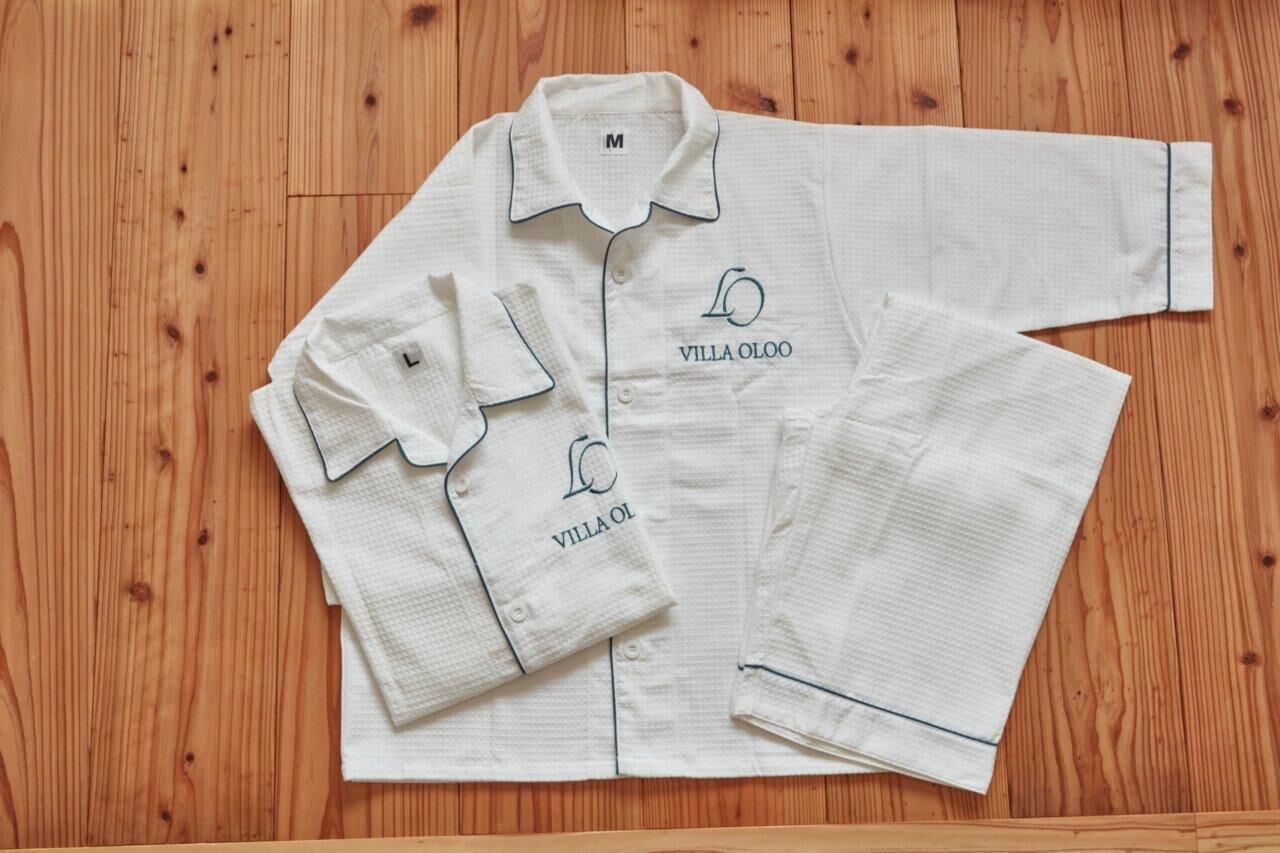 A neatly folded white shirt with the text "VILLA OLOO" on it, placed on a wooden floor.