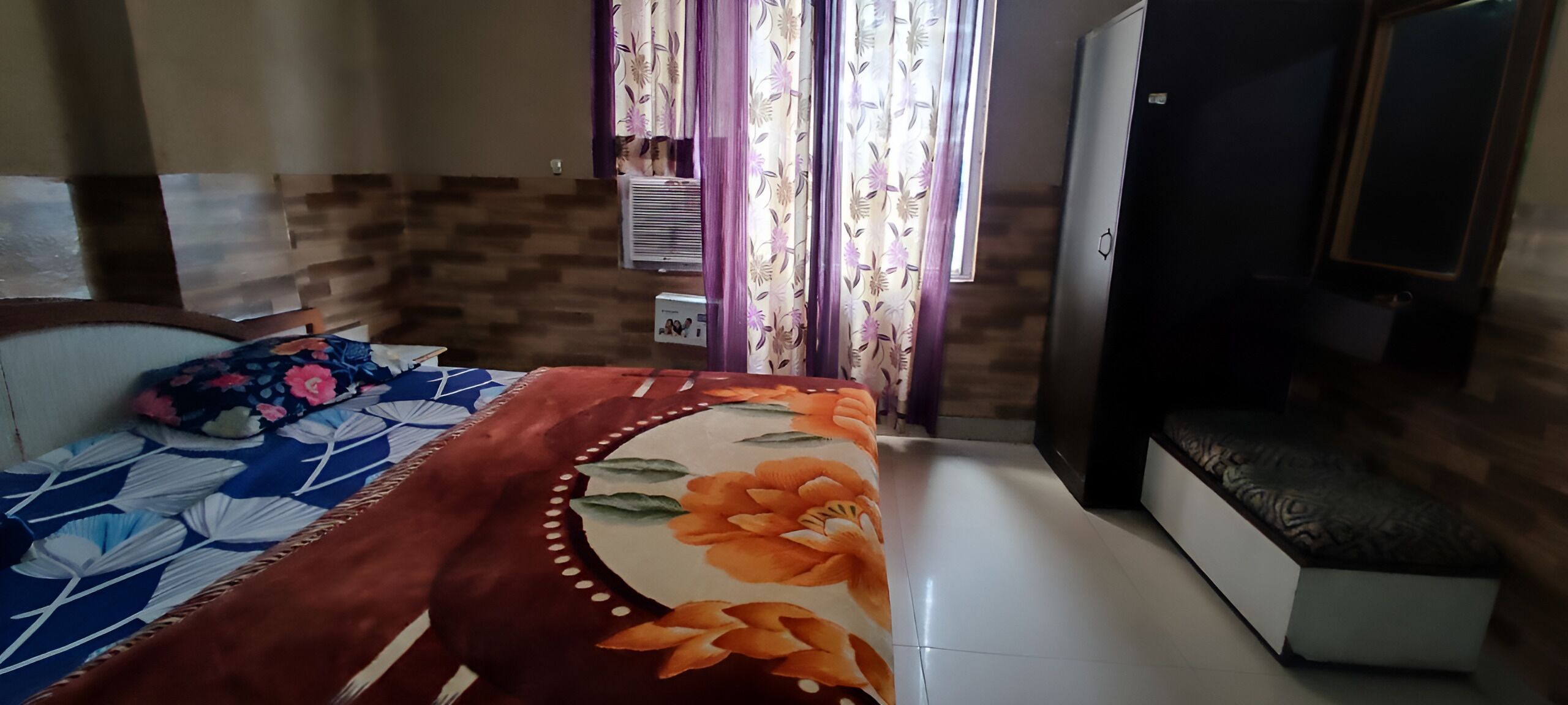 Un dormitorio con cama, un banco, un armario y una ventana con cortinas.