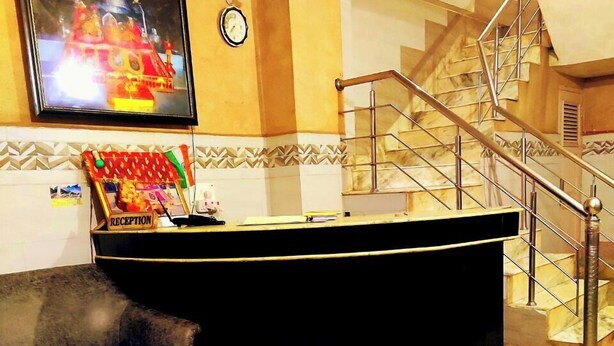 A reception area with a reception desk, a clock, a staircase, and two sofas. - Hotel Ishaan International (Reasi)
