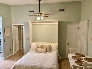 Un dormitorio con cama, ventilador de techo y una mesita pequeña con individuales tejidos.