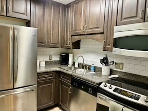 Una cocina con electrodomésticos de acero inoxidable, encimeras de granito y armarios de madera.