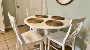 A dining area with a round table, four white chairs, and woven placemats. - Cozy Beach Condo! Safe Complex! (Panama City Beach)