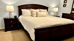 A bedroom with a large bed, two bedside tables with lamps, a dresser, and a mirror. - Cozy Beach Condo! Safe Complex! (Panama City Beach)