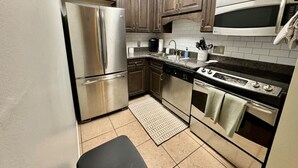A compact kitchen with stainless steel appliances, wooden cabinets, and a tiled backsplash. - Cozy Beach Condo! Safe Complex! (Panama City Beach)