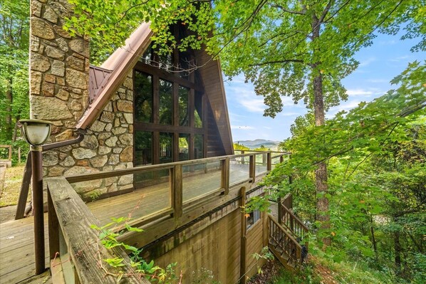 Ein Steinhaus mit Holzterrasse und Glastür, umgeben von Bäumen.
