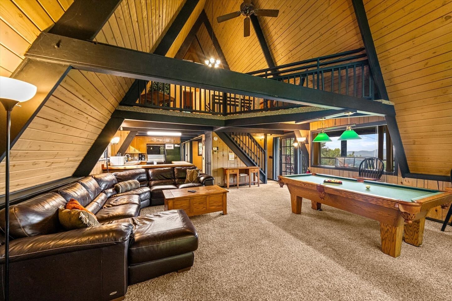 A cozy loft-style room with a pool table, leather sofa, and a staircase leading to an upper level.