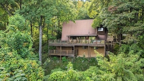 Une cabane dotée d’une terrasse et d’un balcon à l’étage, entourée d’une forêt dense.