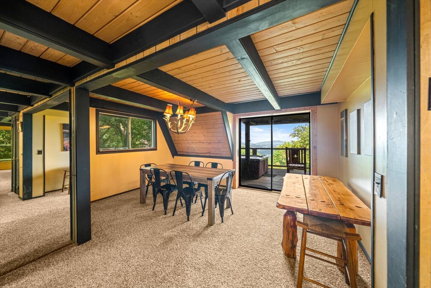 A modern interior with a wooden ceiling, a dining area with a table and chairs, and a view through a glass door to an outdoor deck.