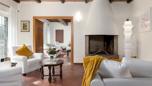 A living room with white sofas, a wooden coffee table, a fireplace, and a view through an open doorway. - Tenuta Francigena 8 Emma Villas (Castelfranco di Sotto)