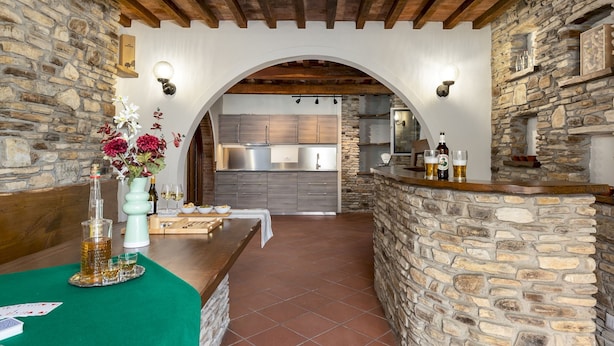 A rustic interior with a stone archway leading to a kitchen, a bar area with a green table, and a wooden ceiling. - Tenuta Francigena 8 Emma Villas (Castelfranco di Sotto)