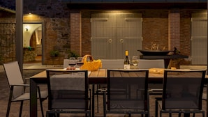 An outdoor dining area with a brick wall, a wooden pergola, and a table set for two with chairs. - Tenuta Francigena 8 Emma Villas (Castelfranco di Sotto)