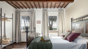 A bedroom with a bed, a bedside table, a window with curtains, a wooden ceiling, and a view of trees outside. - Tenuta Francigena 8 Emma Villas (Castelfranco di Sotto)