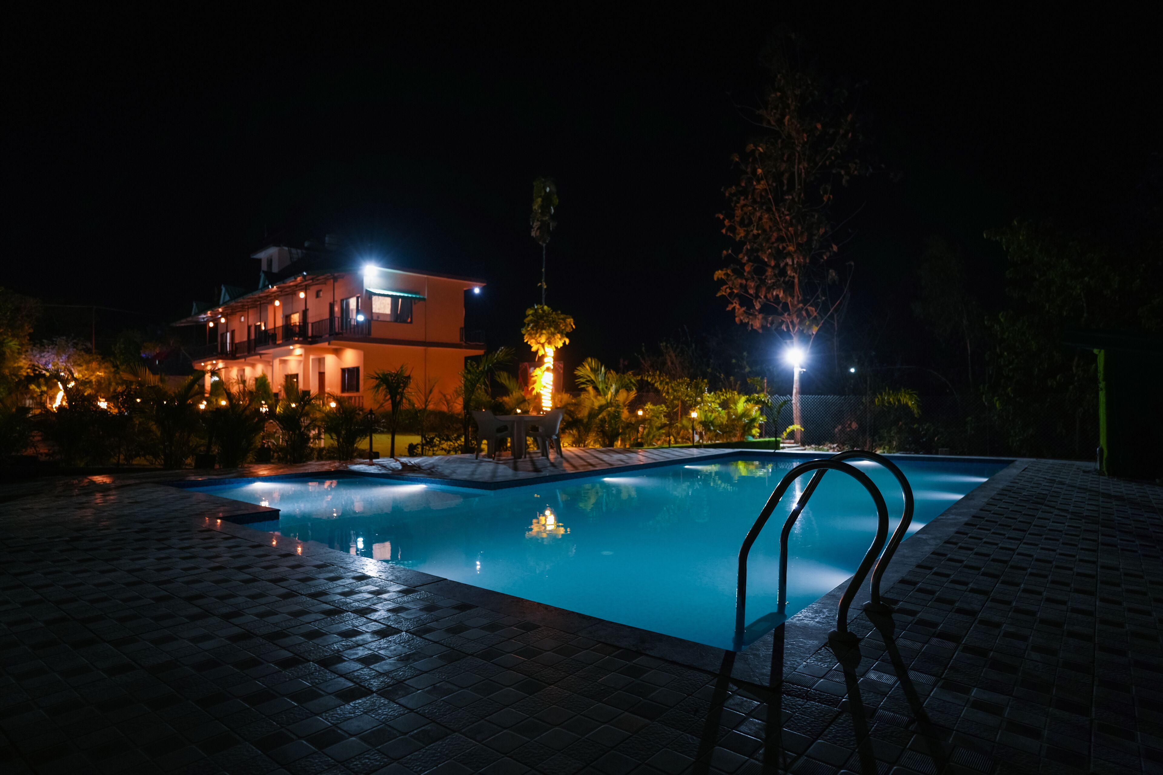 A nighttime swimming pool area with a pool, lounge chairs, and a building in the background.