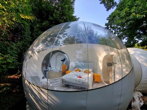 A transparent spherical structure with a bed, a small table, and a chair inside. - Maison Bulle - Absolute Peace and Quiet (Lindry)