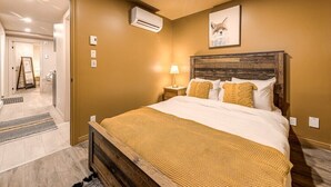 Ein Schlafzimmer mit einem hölzernen Kopfteil, einem Bett mit weißer Bettwäsche und einer gelben Tagesdecke, einer Klimaanlage und einem gerahmten Bild an der Wand.