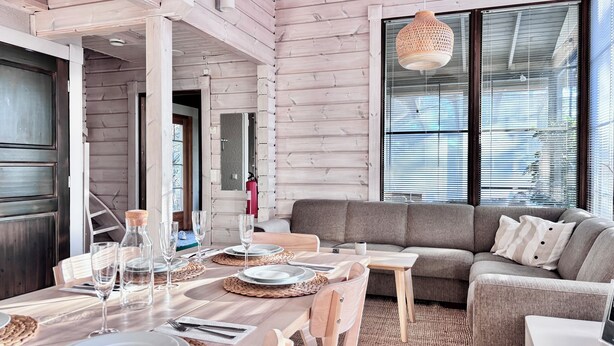 Un intérieur moderne avec un coin repas en bois, un canapé gris et de grandes fenêtres.