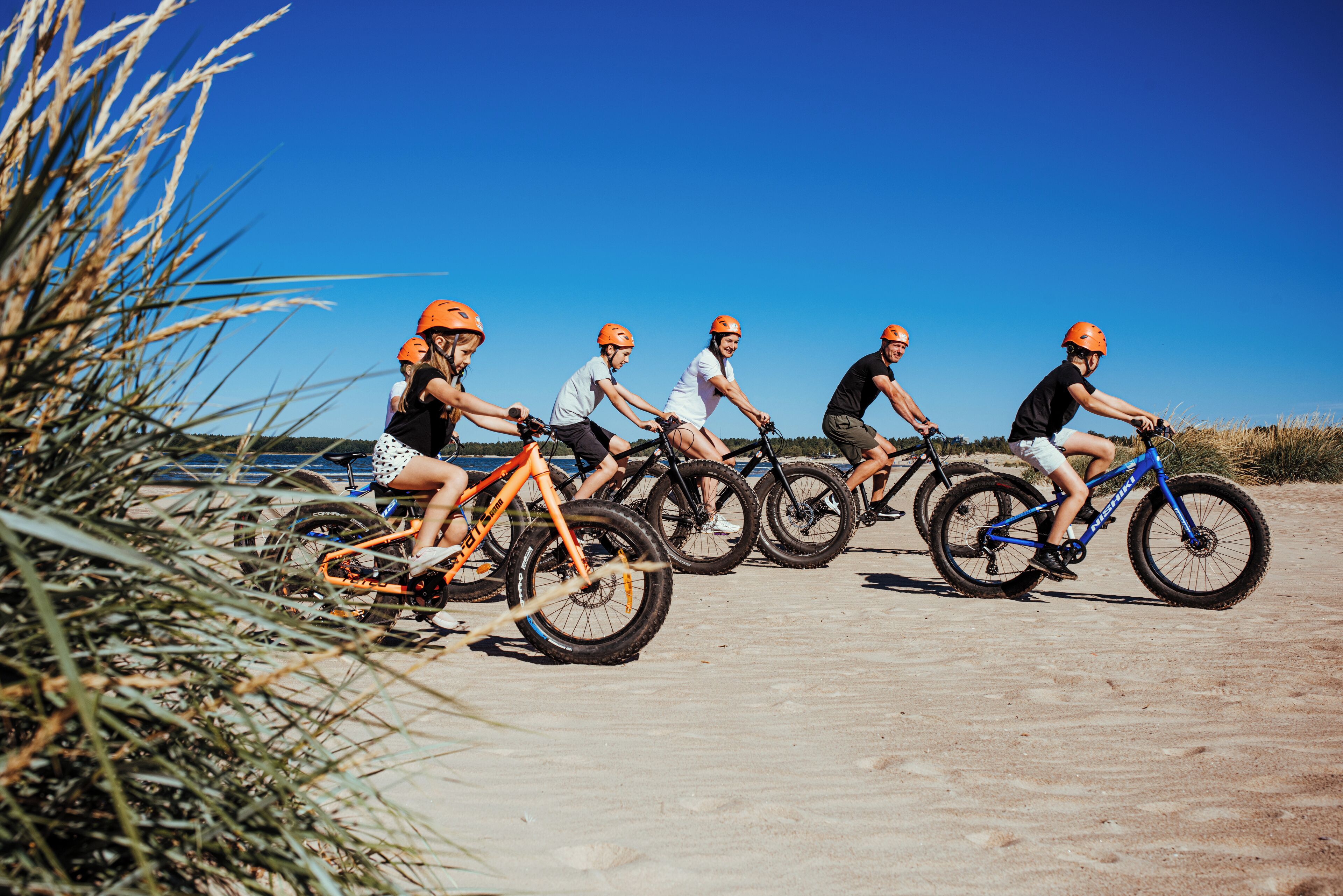 A group of people riding bicycles on a sandy path with a clear blue sky in the background.