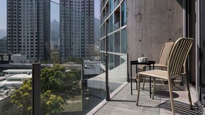 A balcony with a view of high-rise buildings, a glass partition, and a chair.