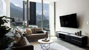 A modern living room with a sofa, coffee table, and TV. It features a large window with a mountain view.