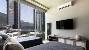 A modern hotel room with a large bed, a TV, and a view of a cityscape and mountains. - Huasteca Mountain Views, Pool, Gym & Balcony (Santa Catarina)