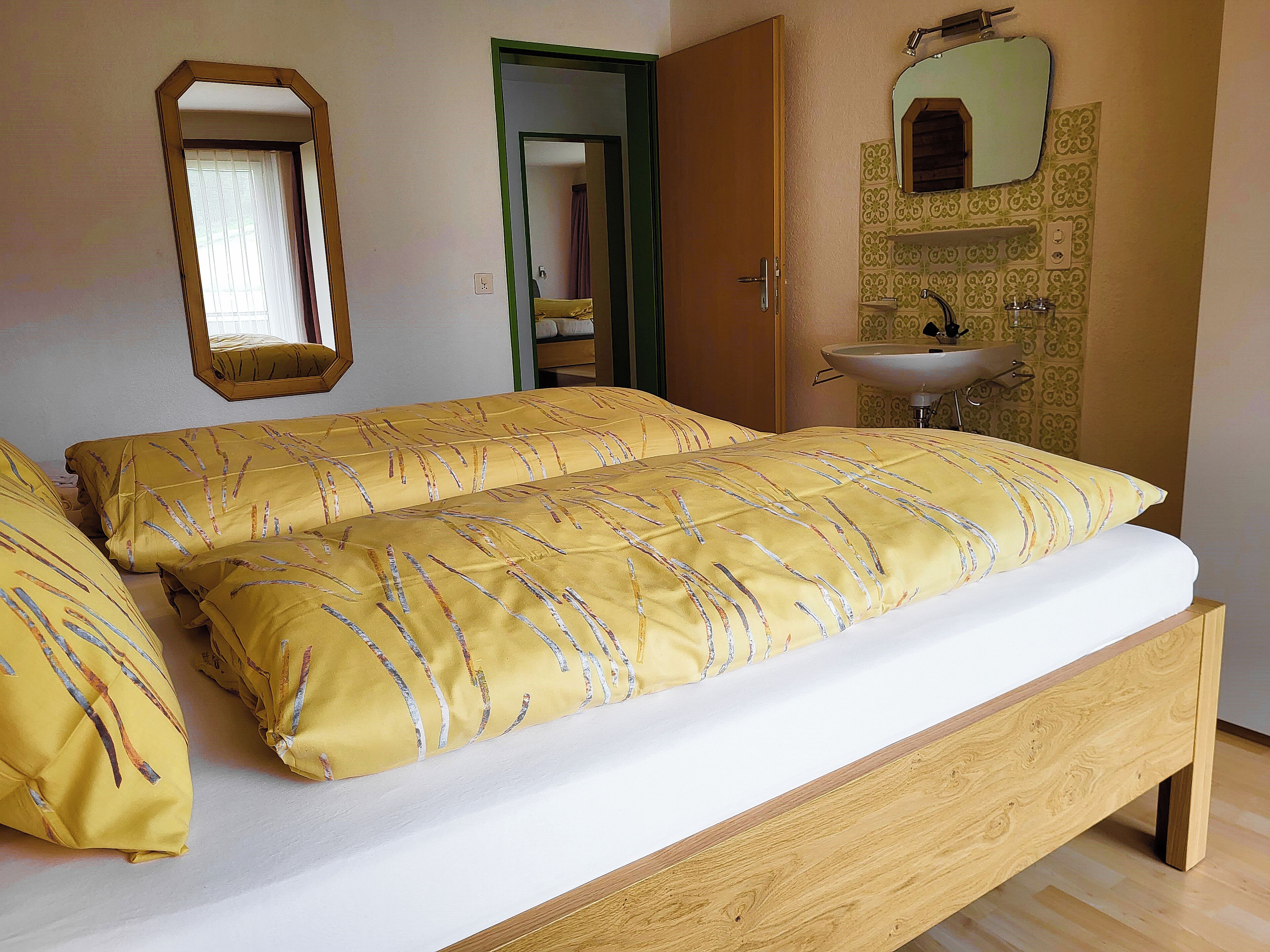 A bedroom with a wooden bed, yellow pillows, a mirror, and a bathroom with a sink.