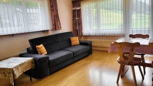 A living room with a black sofa, wooden dining table, and chairs. - Apartments Atlas (Saas Grund)