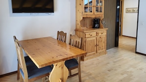 A wooden dining table with chairs, a television mounted on the wall, and a wooden cabinet with drawers. - Apartments Atlas (Saas Grund)