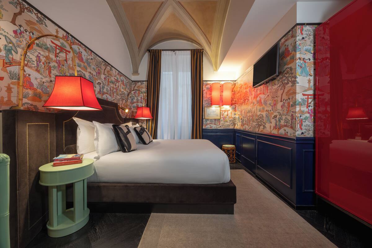 A hotel room with a large bed, two bedside lamps, a small round table, and a television mounted on the wall.