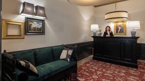 A room with a green sofa, a black reception desk, and a red patterned carpet. - V Collection Condotti (Rome)