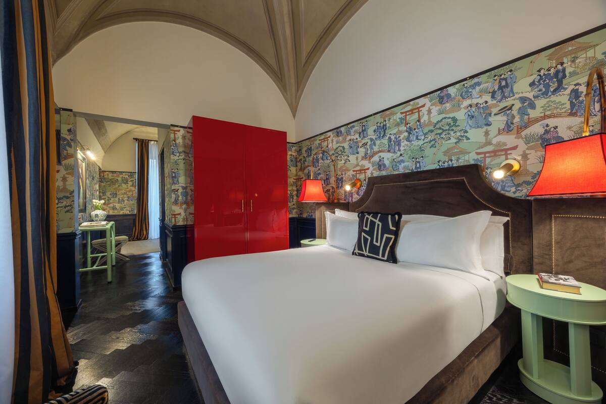 A hotel room with a large bed, red wardrobe, and traditional Asian-style wallpaper.
