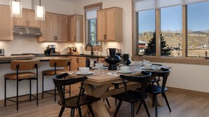 A modern kitchen with wooden cabinets, a large window, and a dining area with black chairs and a wooden table. - Downtown Fraser| Hot tub |Walkable (Fraser)