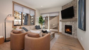 A modern living room with a fireplace, a flat-screen TV, and a large window. - Downtown Fraser| Hot tub |Walkable (Fraser)