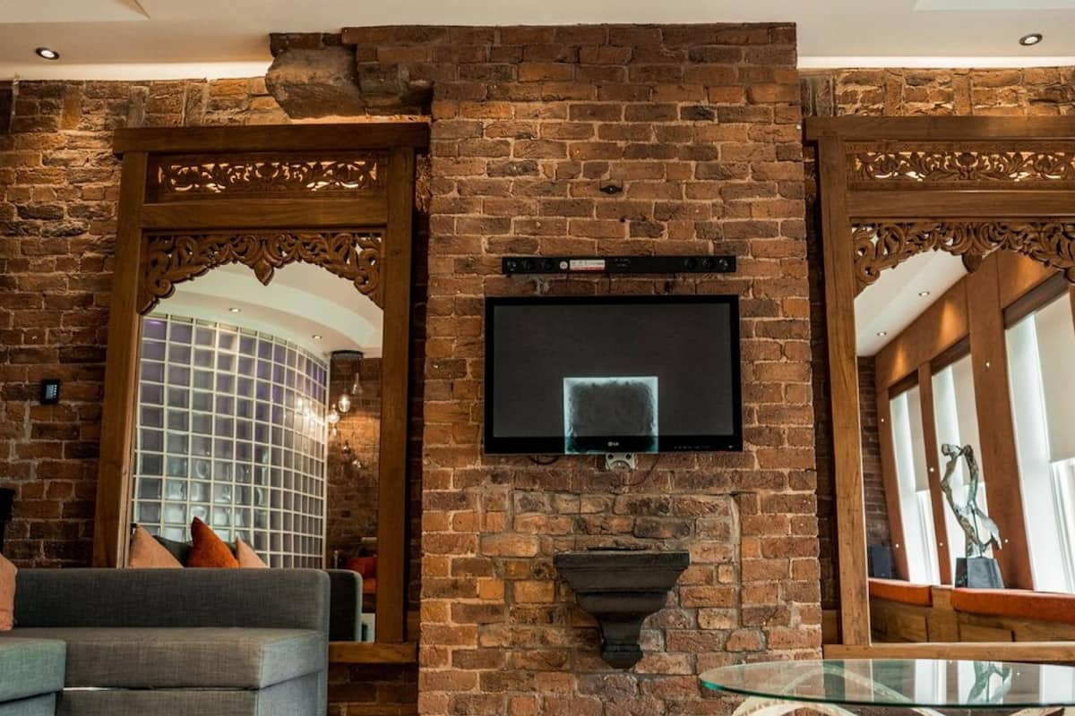 A room with a brick wall, a mounted TV, a glass table, and a sofa.