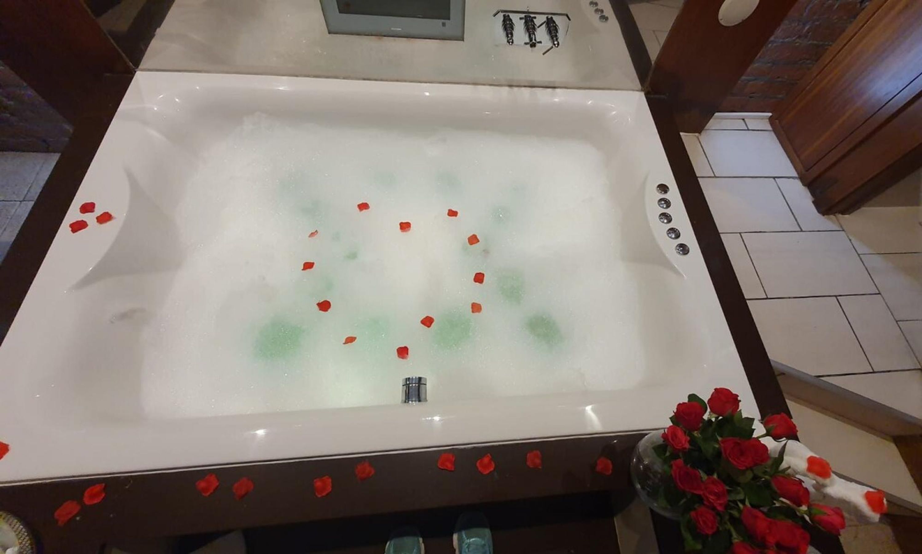 A bathtub with rose petals and a bouquet of roses.