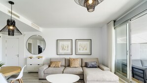 Una sala de estar moderna con un sofá seccional color beige, un espejo redondo y dos obras de arte enmarcadas en la pared.