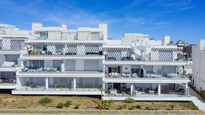 Un moderno edificio residencial de varios pisos con balcones, mobiliario exterior y una vista despejada del entorno.