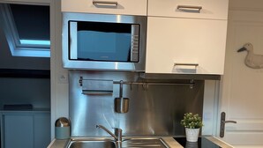Une cuisine compacte dotée d’un four à micro-ondes encastré, d’un évier en acier inoxydable et de meubles de rangement blancs.