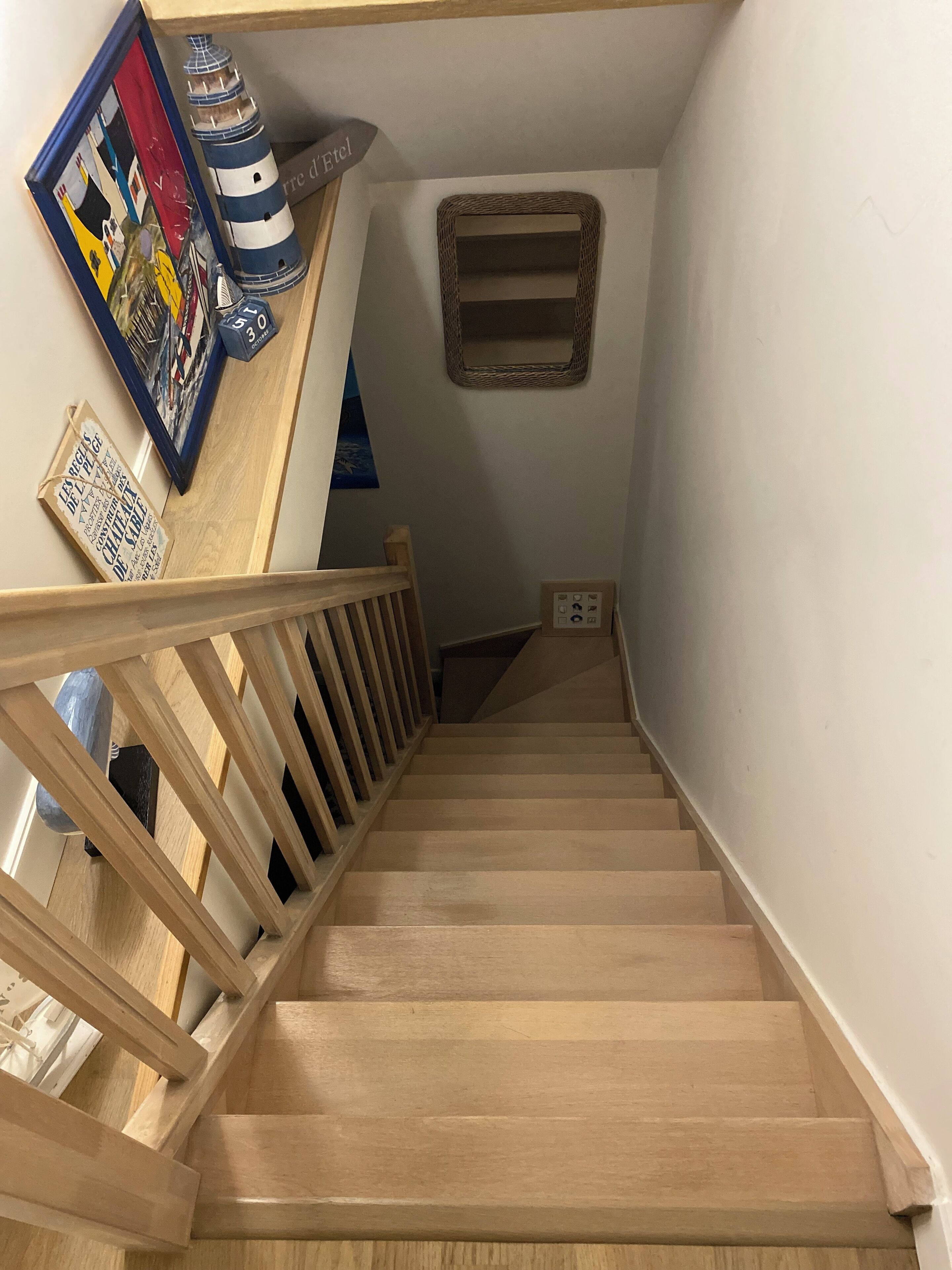 A wooden staircase with a railing, a framed painting, and a small mirror on the wall.