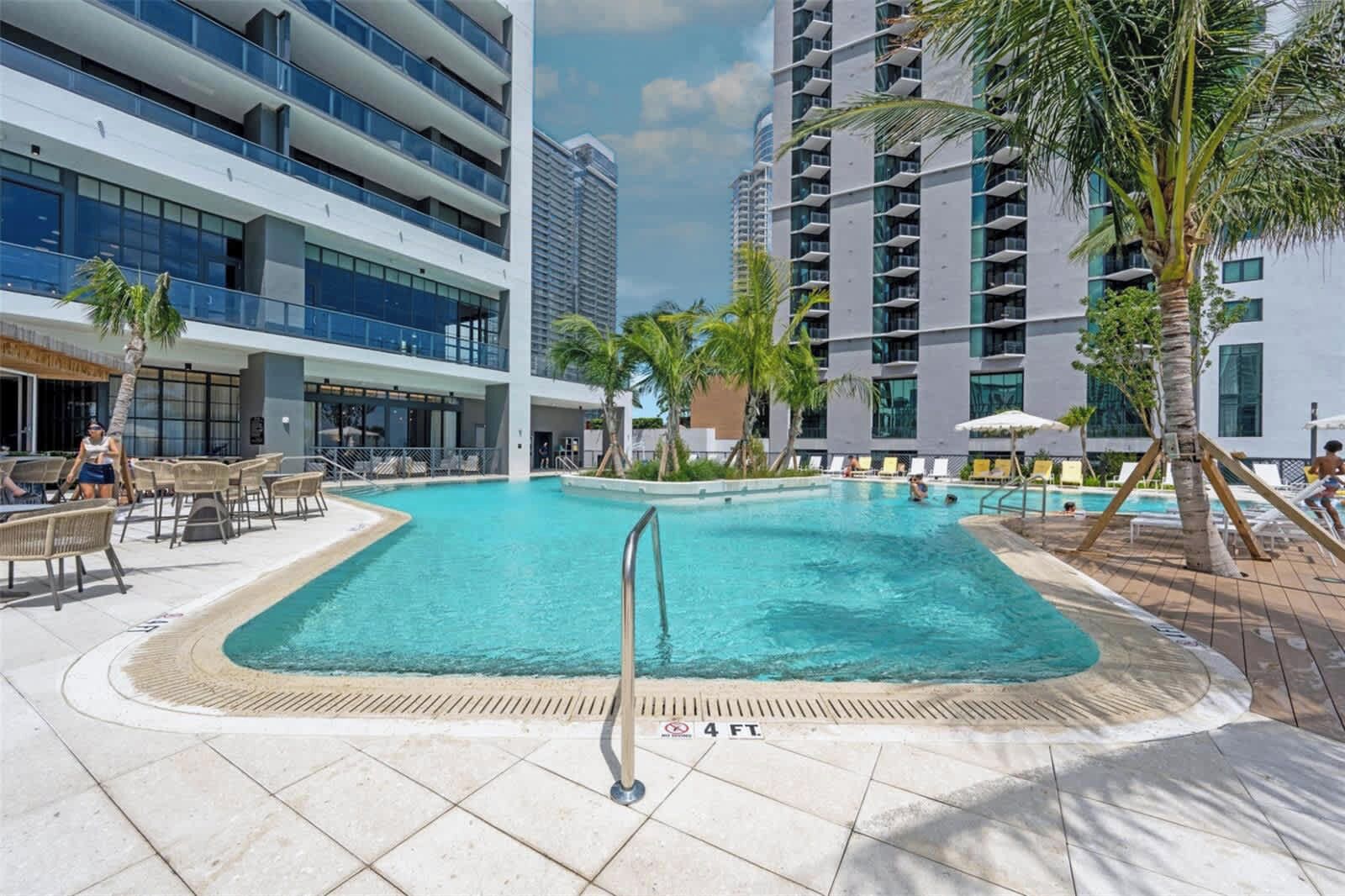 Et moderne hotel med central pool, udendørs siddepladser og palmer.