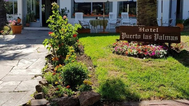 A hotel entrance with a sign reading "Hotel Puerto las Palmas," outdoor seating with umbrellas, and a well-maintained garden. - Hotel Puerto Las Palmas (Punta del Este)