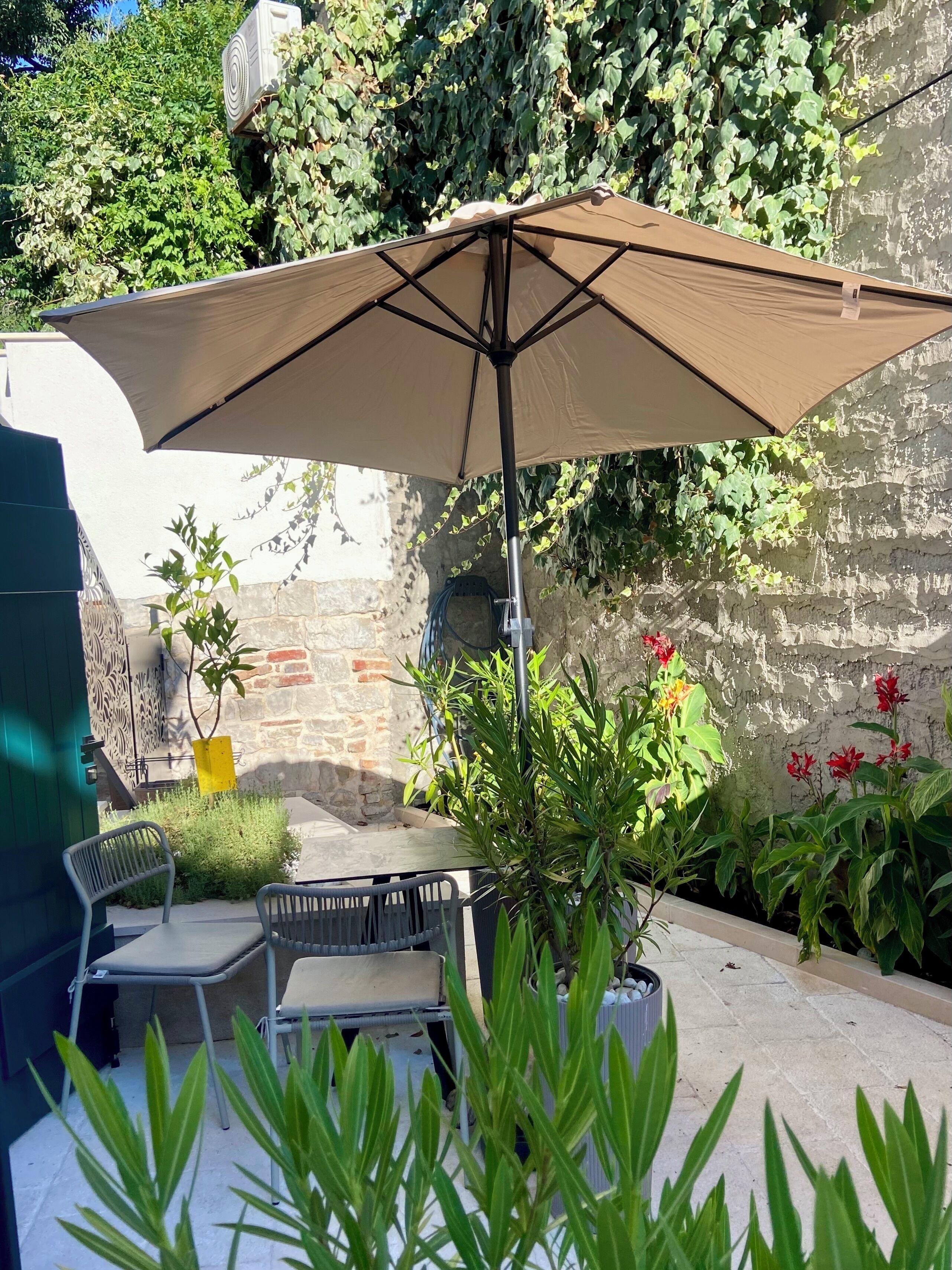 Un patio al aire libre con una mesa y sillas, rodeado de plantas y un muro.